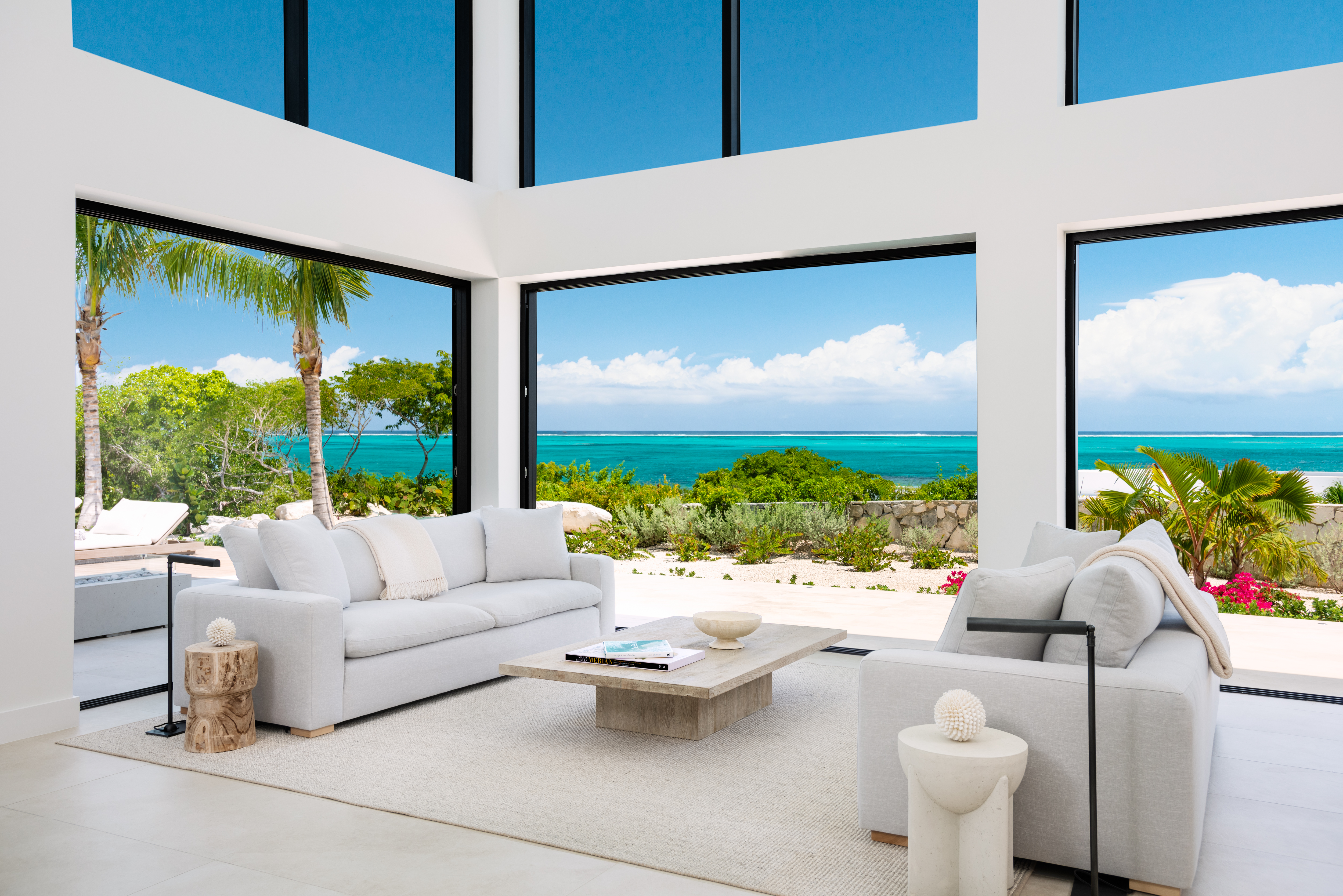 Living room with floor-to-ceiling glass opening to the sea and white sofas