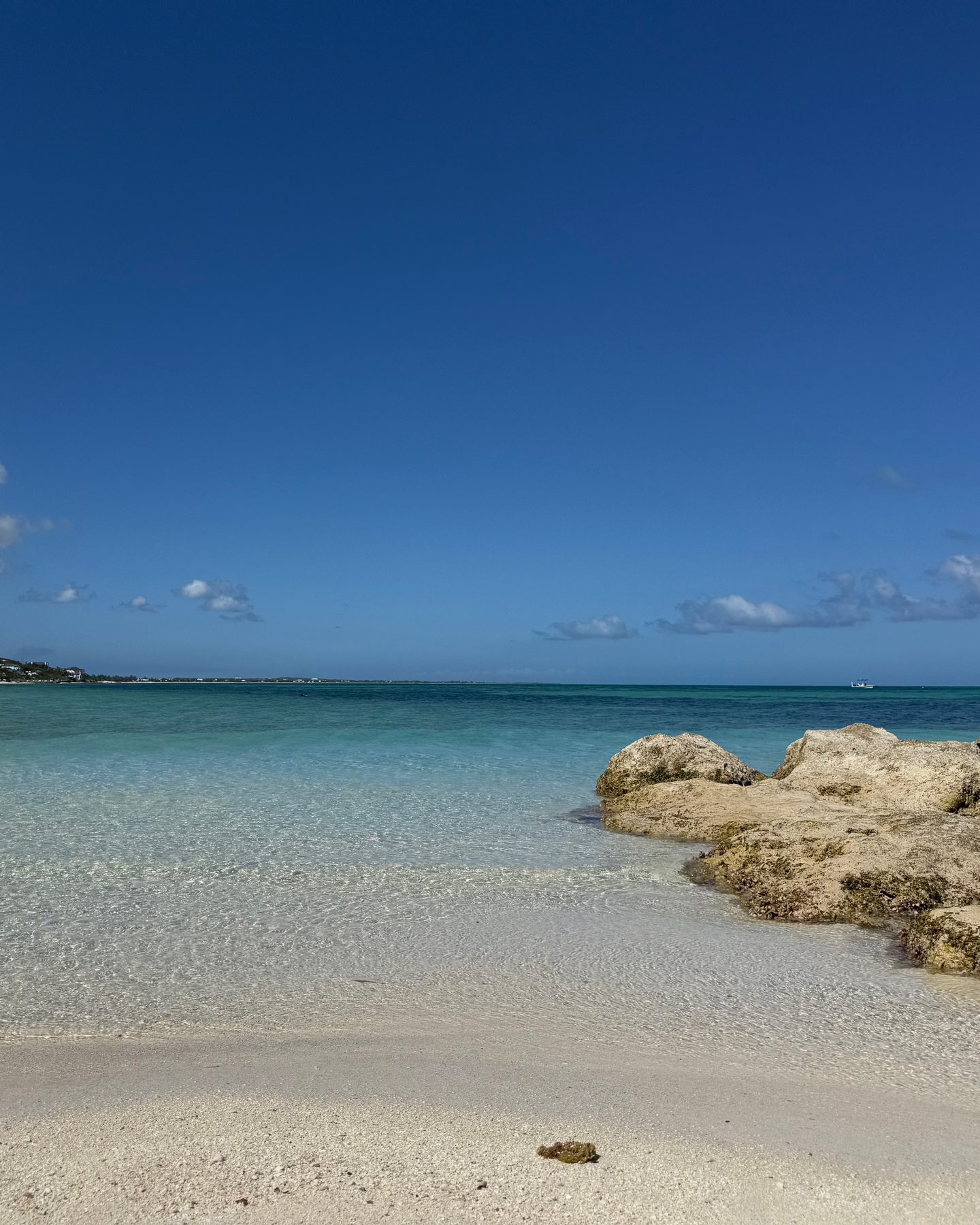 The calm, snorkel-clear turquoise cove and white sand of Babalua Beach, with limestone rocks and the north shore villas in the distance, near Beachwood Villa in Providenciales Turks and Caicos