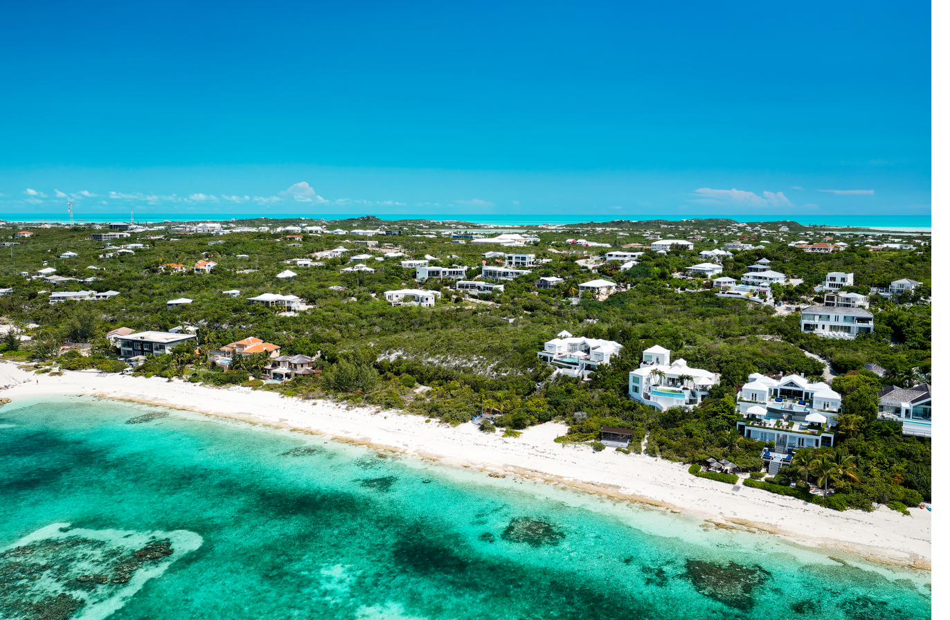 Wide aerial view of the Providenciales north shore coastline with white sand beaches, coral reefs, and turquoise water typical of the Bight beach area