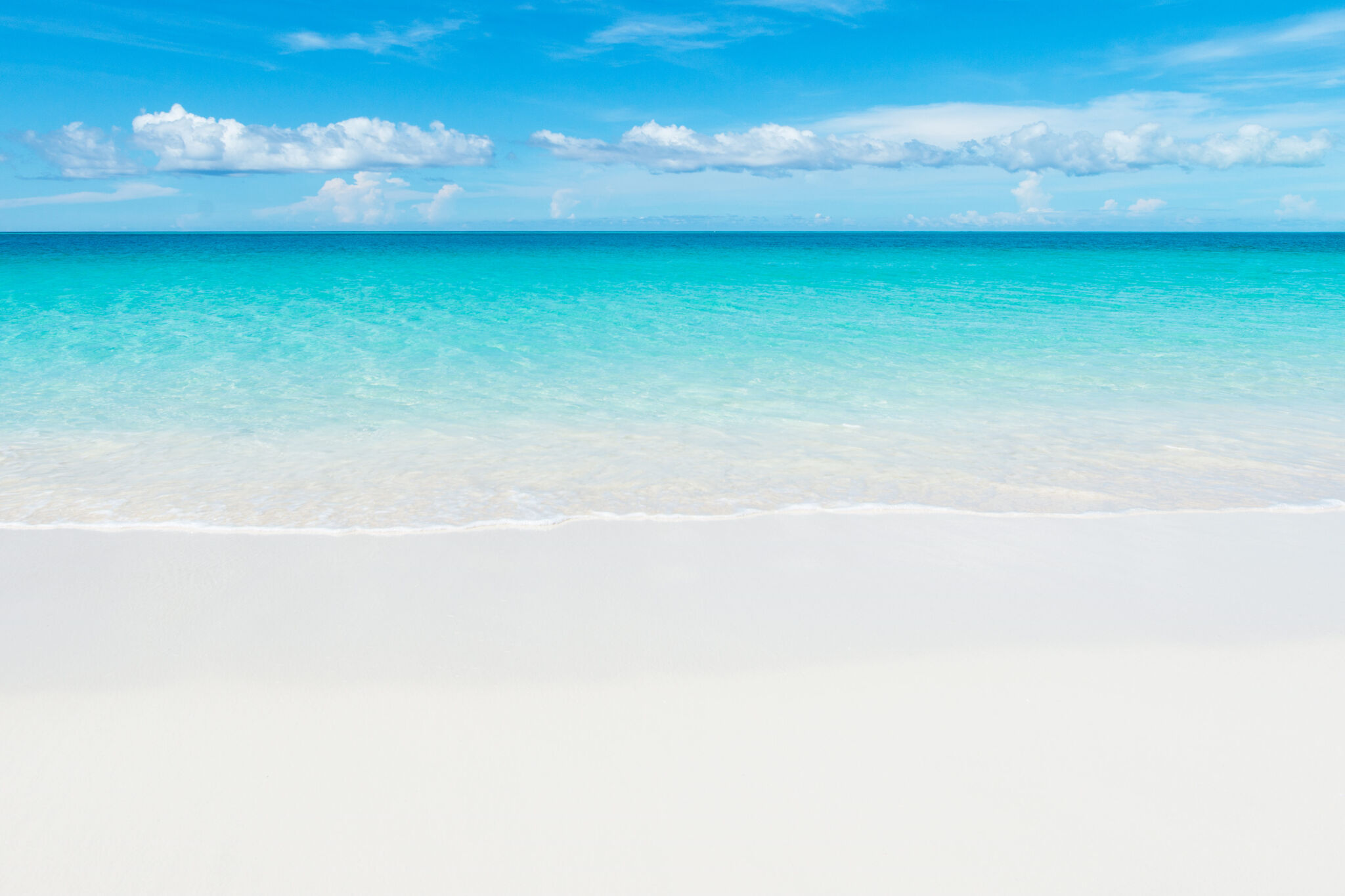Calm turquoise water meeting pristine white sand under a blue sky on a Providenciales beach, Turks and Caicos