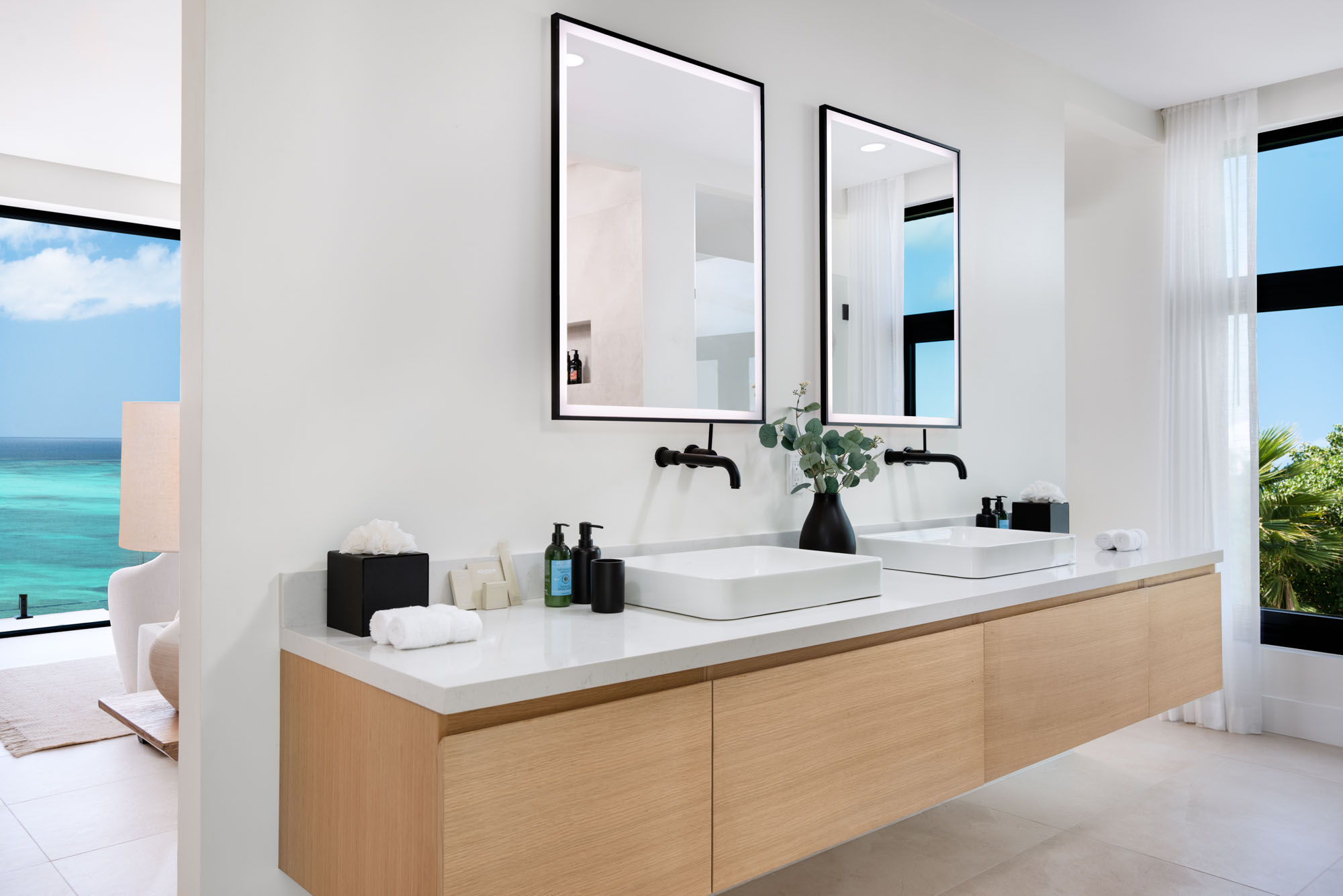 Master ensuite at Beachwood Villa with twin floating oak vanities, vessel sinks, matte black wall-mounted fixtures, and ocean view through the open doorway