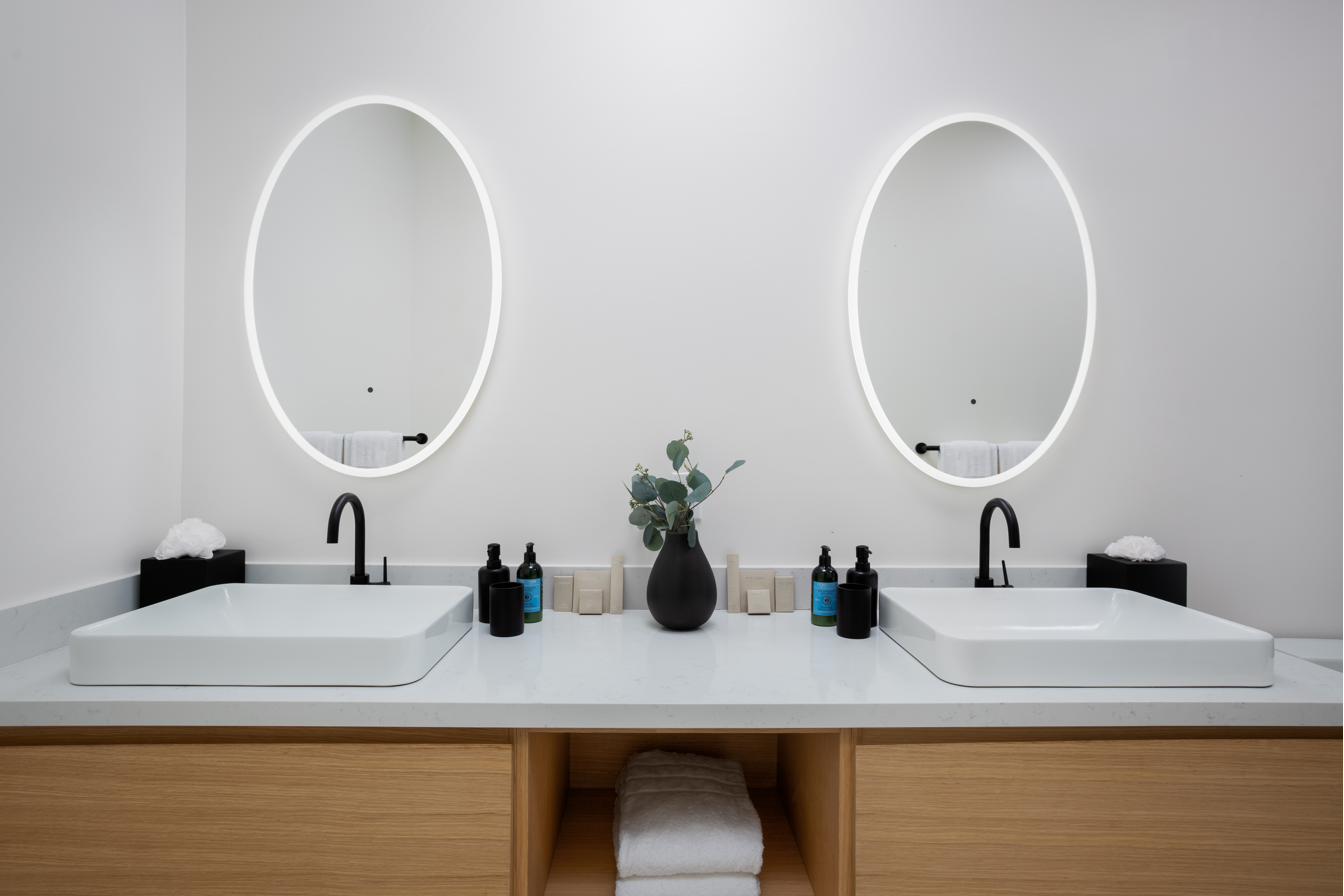 Reef Suite ensuite at Beachwood Villa with oval LED-lit mirrors, double white vessel sinks, floating oak vanity, matte black fixtures, and eucalyptus stems in Providenciales Turks and Caicos