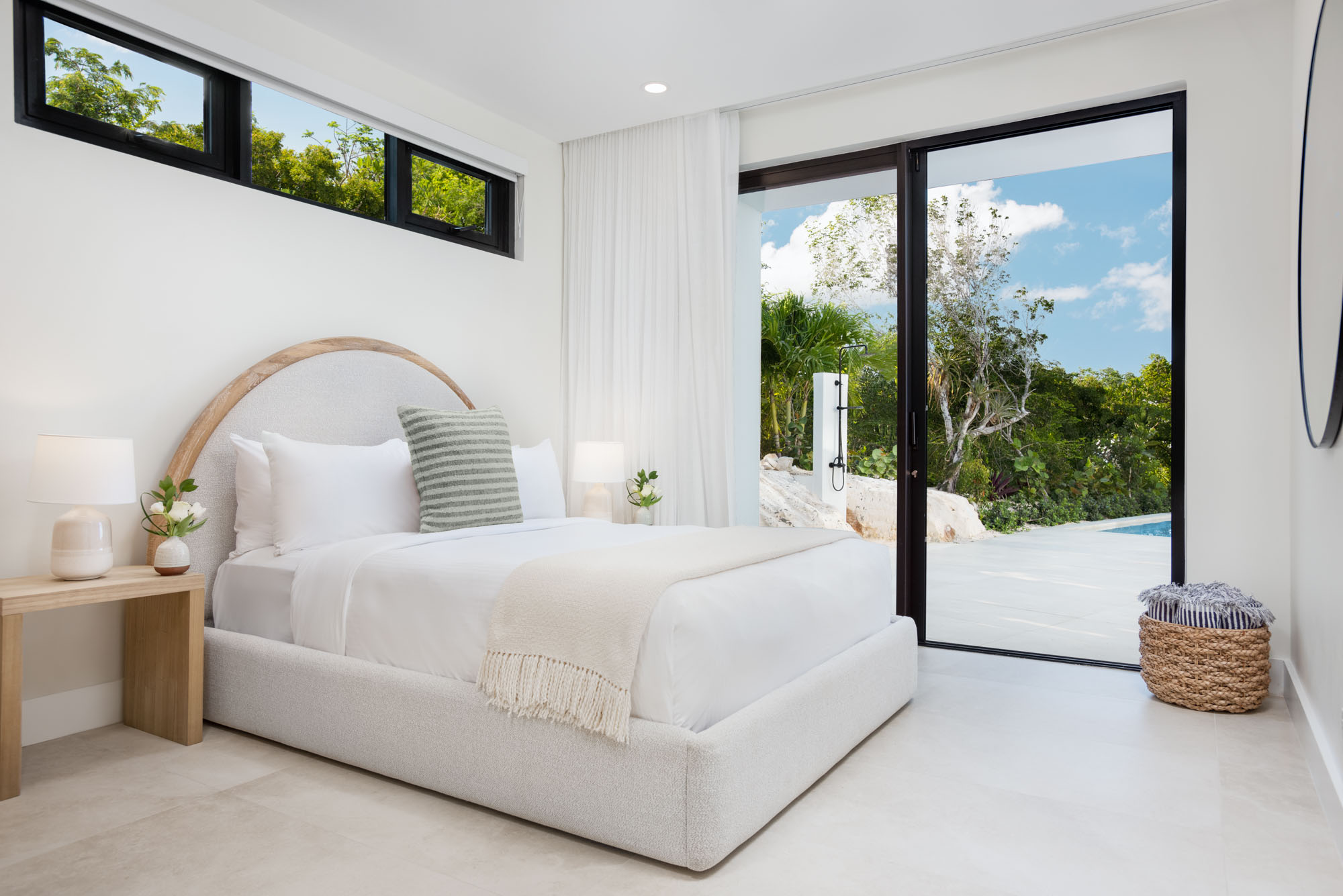The Garden Suite at Beachwood Villa with queen bed, arched boucle headboard, transom windows, and sliding glass door opening to the pool deck and outdoor shower