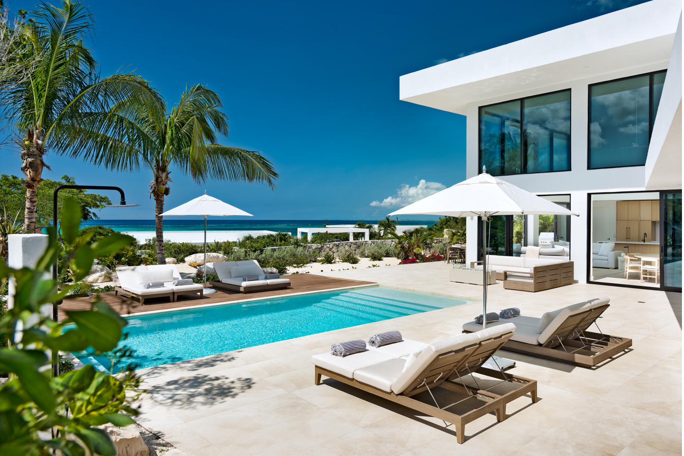 Beachwood Villa pool deck with twin daybeds, palm trees framing the modernist architecture, and the turquoise Caribbean visible beyond in Providenciales Turks and Caicos
