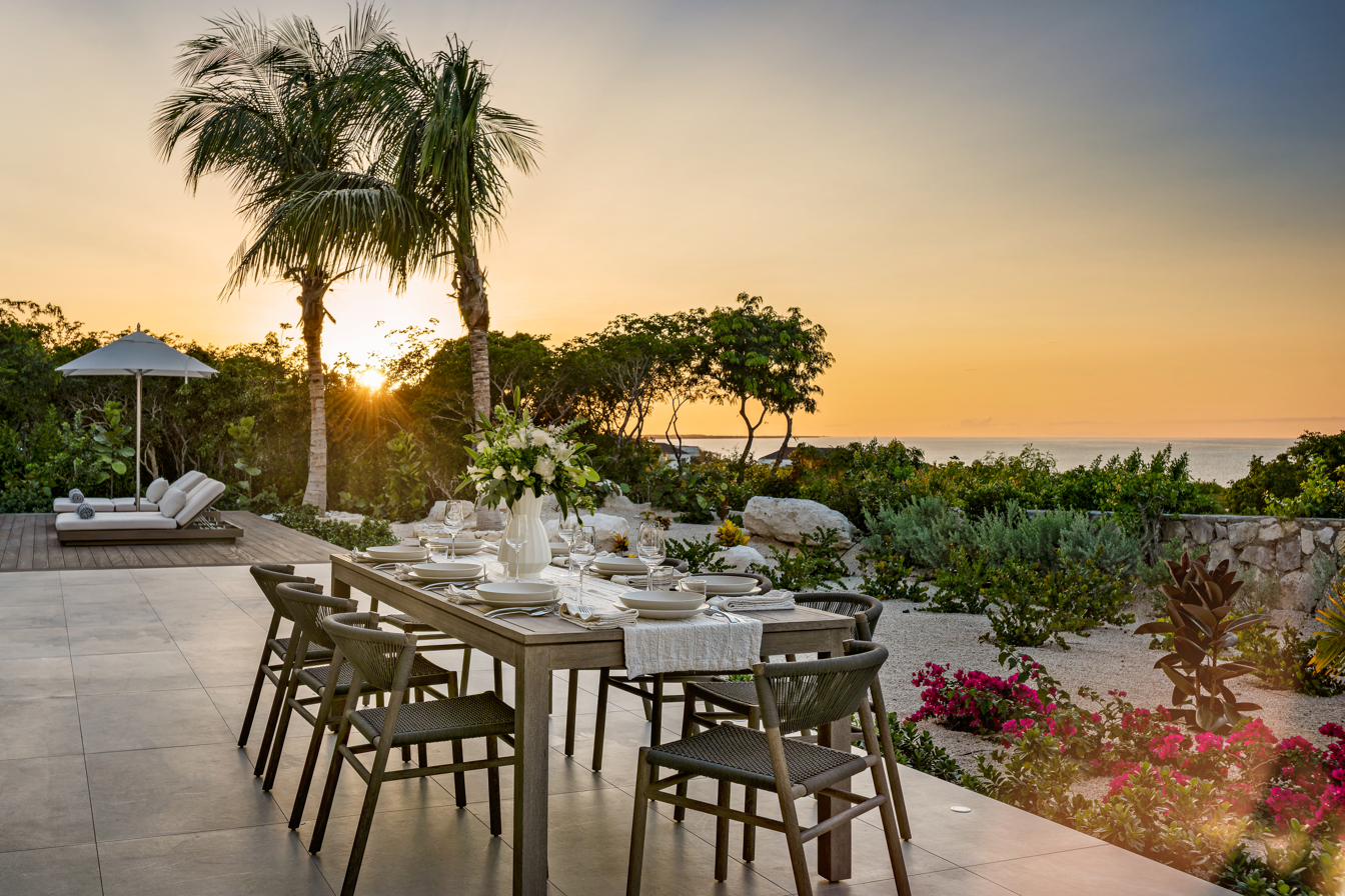 Outdoor dinner table set for golden hour at Beachwood Villa with palm trees, tropical gardens, and ocean views over Providenciales Turks and Caicos