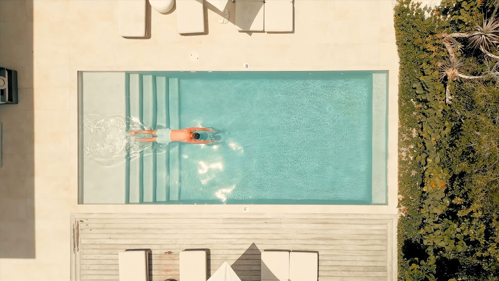 Top-down view of a guest swimming laps in the private pool at Beachwood Villa, framed by loungers and tropical greenery in Providenciales Turks and Caicos