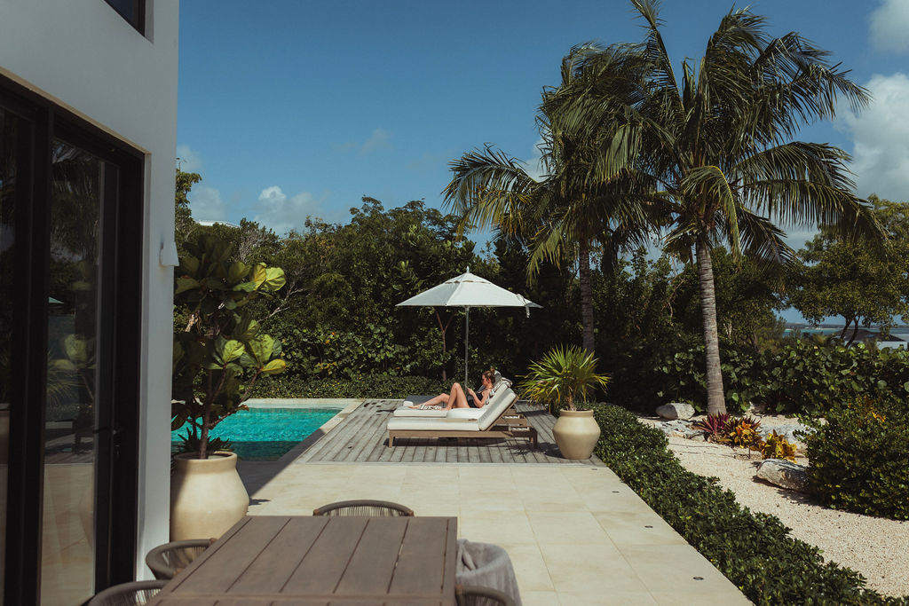 A guest relaxing on a lounger by the pool deck under palms in the quiet morning light at Beachwood Villa, Providenciales Turks and Caicos