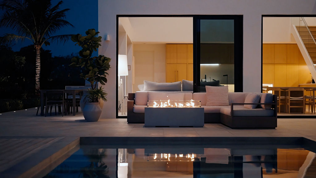 The lit fire pit and outdoor sofa on the terrace at dusk, the villa glowing behind and reflected in the pool at Beachwood Villa