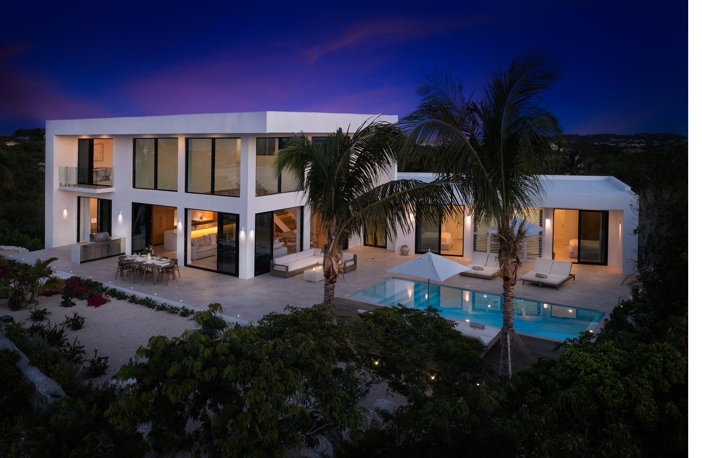 Beachwood Villa at twilight, glowing from within, with the pool lit and palms framing the modernist architecture in Providenciales, Turks and Caicos