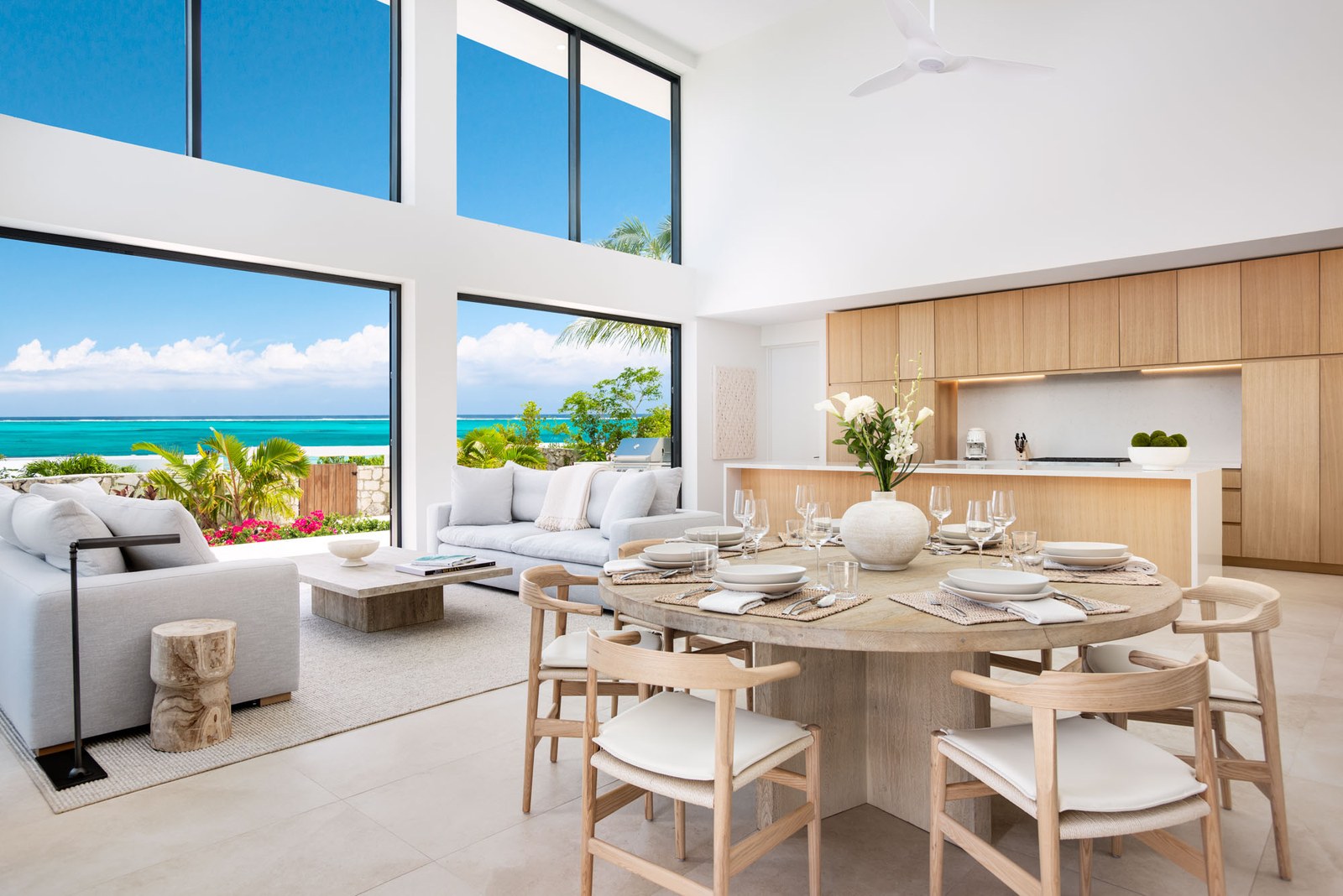 Beachwood Villa interior — open-concept great room with 20-foot ceilings, floor-to-ceiling windows, oak round dining table for ten, custom oak kitchen, and sweeping turquoise ocean views in Providenciales Turks and Caicos