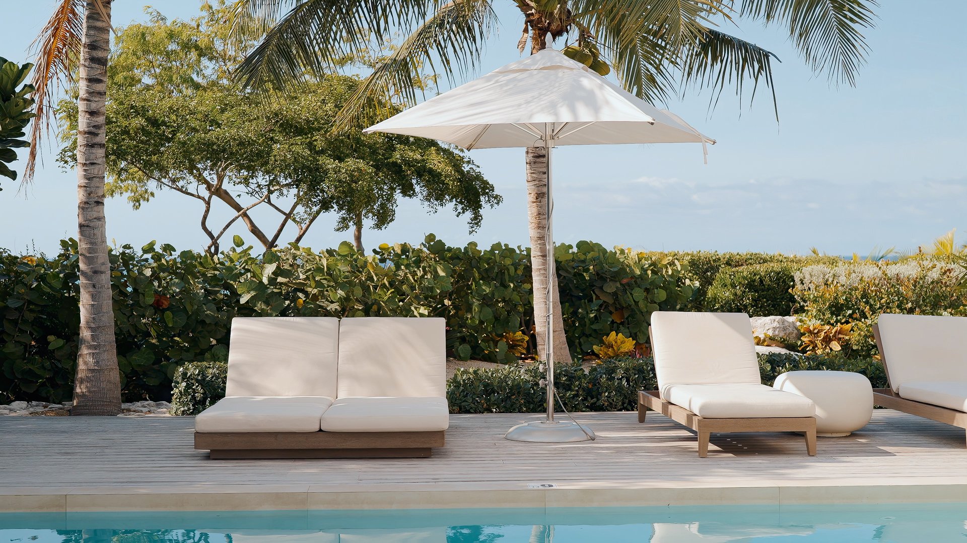 Beachwood Villa pool with white pool sofas, sun loungers, palm trees, and tropical foliage with ocean view in Providenciales Turks and Caicos