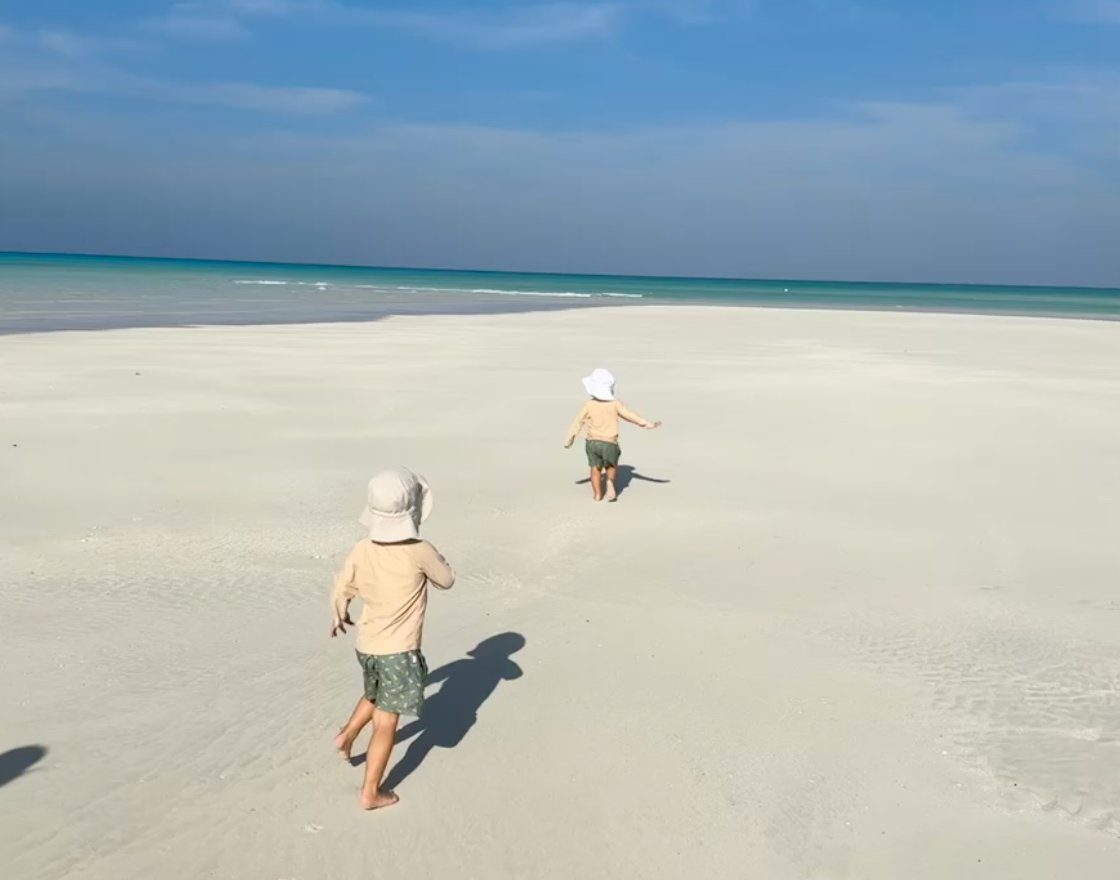 Two young children running across an empty white-sand beach toward the turquoise water in Providenciales, Turks and Caicos